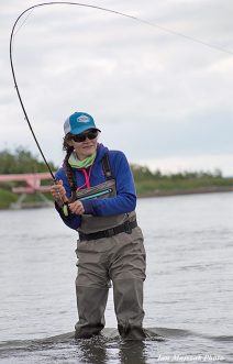 Man with backpack casting fly fishing pole at river - Stock Image