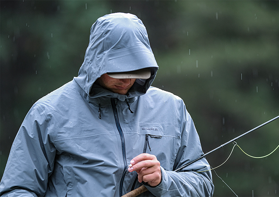 Angler inspecting his fly while wearing a Skwala Carbon Wading Jacket