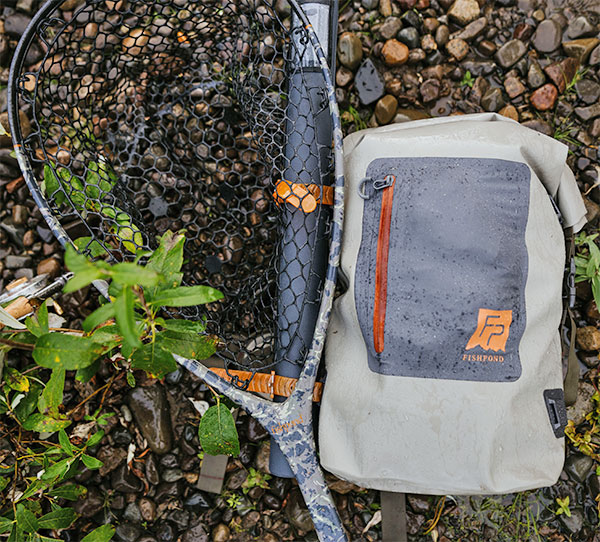 Fishpond Wind River Roll-Top Dry Backpack and Nomad net laying on the rocks
