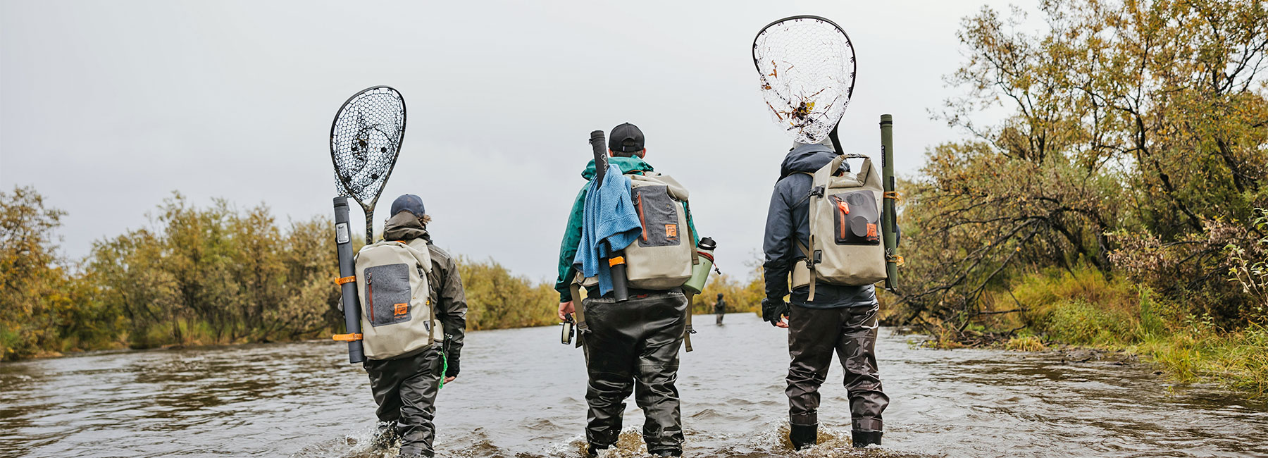 Three anglers walking wearing the Fishpond Wind River Roll-Top Dry Backpack